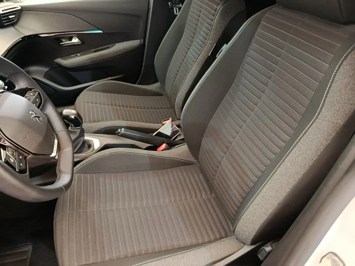 Vue intérieure côté conducteur de la Peugeot 208 2023, sièges tissu gris et volant cuir multifonctions noir.