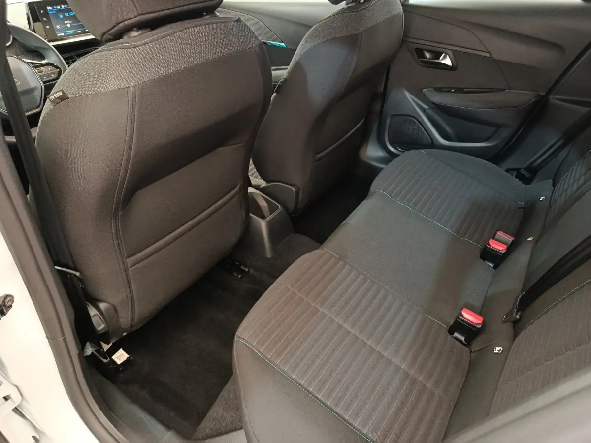Vue intérieure arrière côté gauche de la Peugeot 208 2023 avec sièges tissu noir et ceintures rouges visibles.