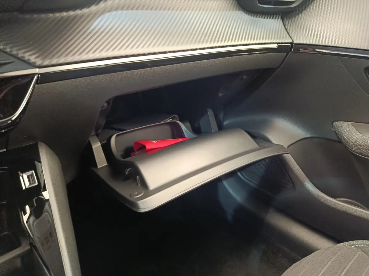 Intérieur de la Peugeot 208 PureTech 75 S&S Style 2023, vue sur la boîte à gants ouverte côté passager avec un objet rouge à l'intérieur.