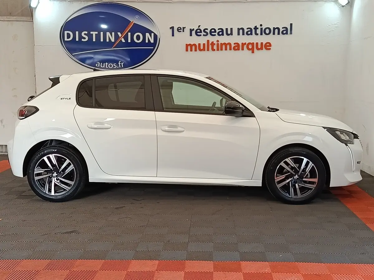 Profil droit de la Peugeot 208 PureTech 75 S&S Style blanche, avec jantes alliage et rétroviseurs noirs, en intérieur showroom.