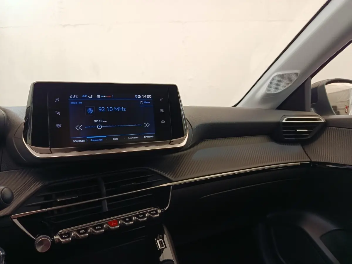 Vue intérieure côté passager du tableau de bord noir de la Peugeot 208 2023 avec écran tactile central allumé.
