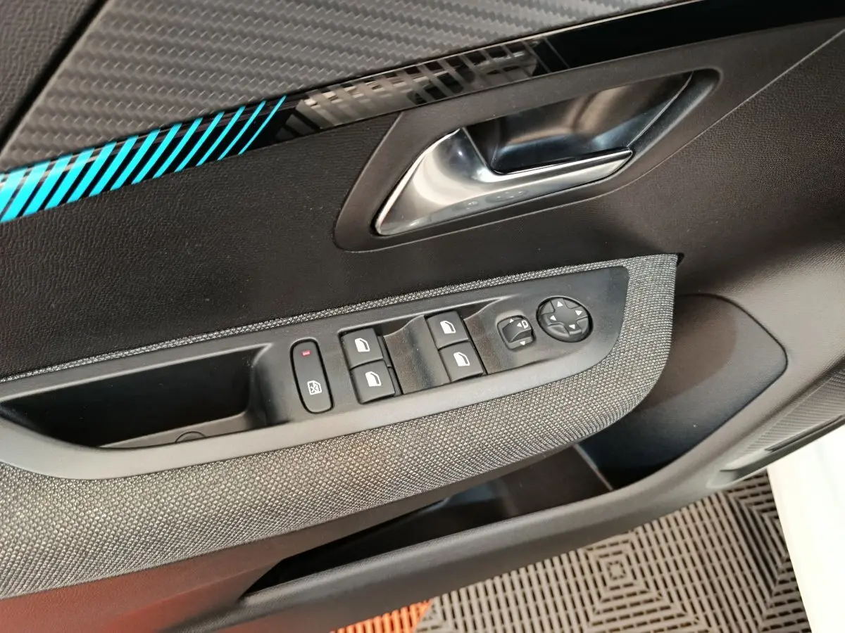 Gros plan sur la porte côté conducteur de la Peugeot 208 2023, montrant les commandes des vitres et le décor carbone avec liseré bleu.