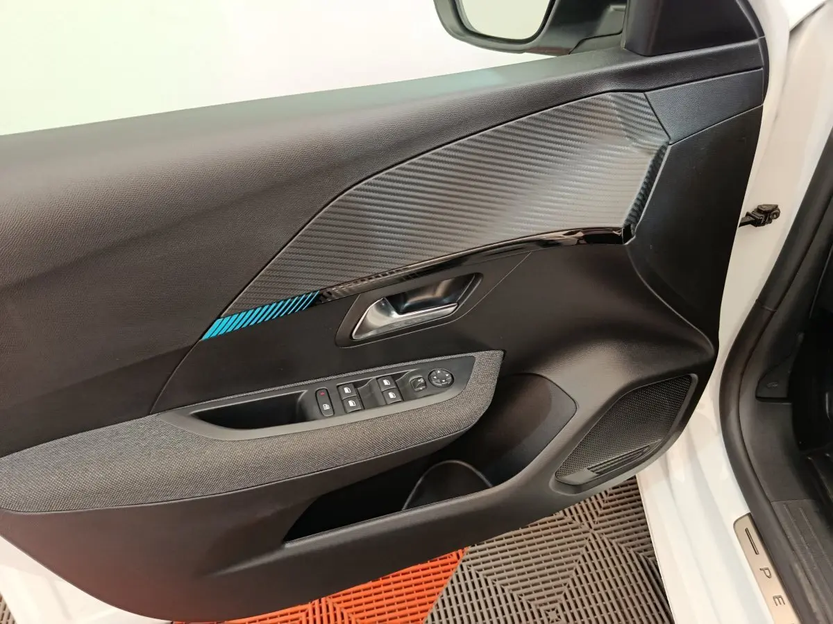 Vue rapprochée de la porte avant gauche blanche d’une Peugeot 208 avec insert décoratif noir et bleu et commandes électriques.
