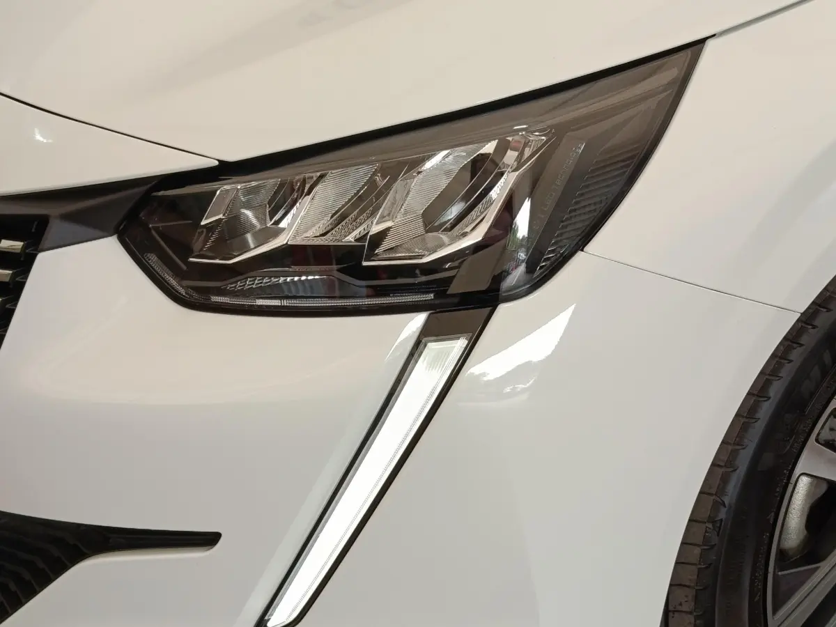 Gros plan sur le phare avant gauche blanc du Peugeot 208 2023 avec feu de jour LED en forme de griffes.