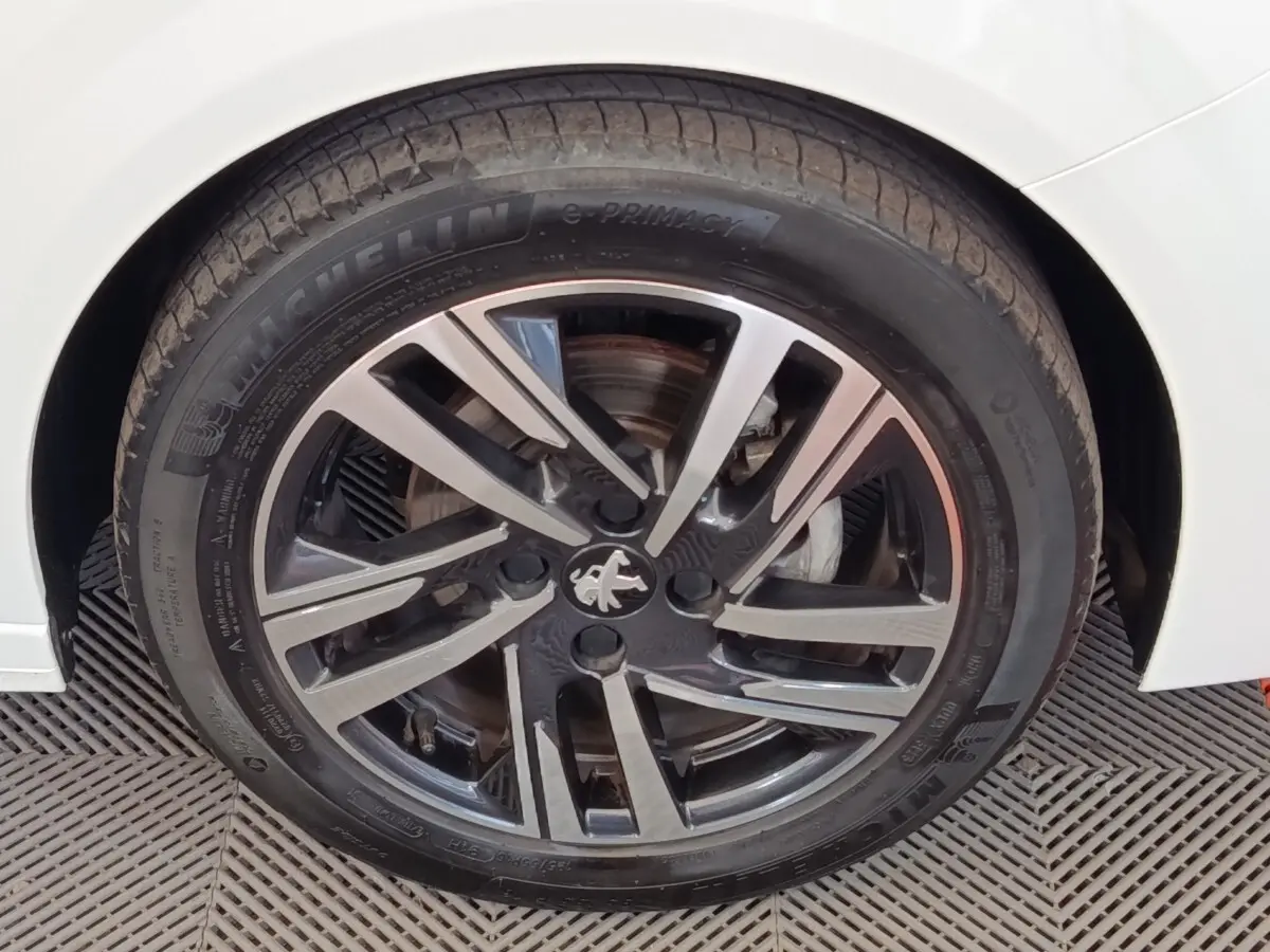 Gros plan sur la roue avant droite d'une Peugeot 208 blanche avec jante alliage noire et argentée au design moderne.