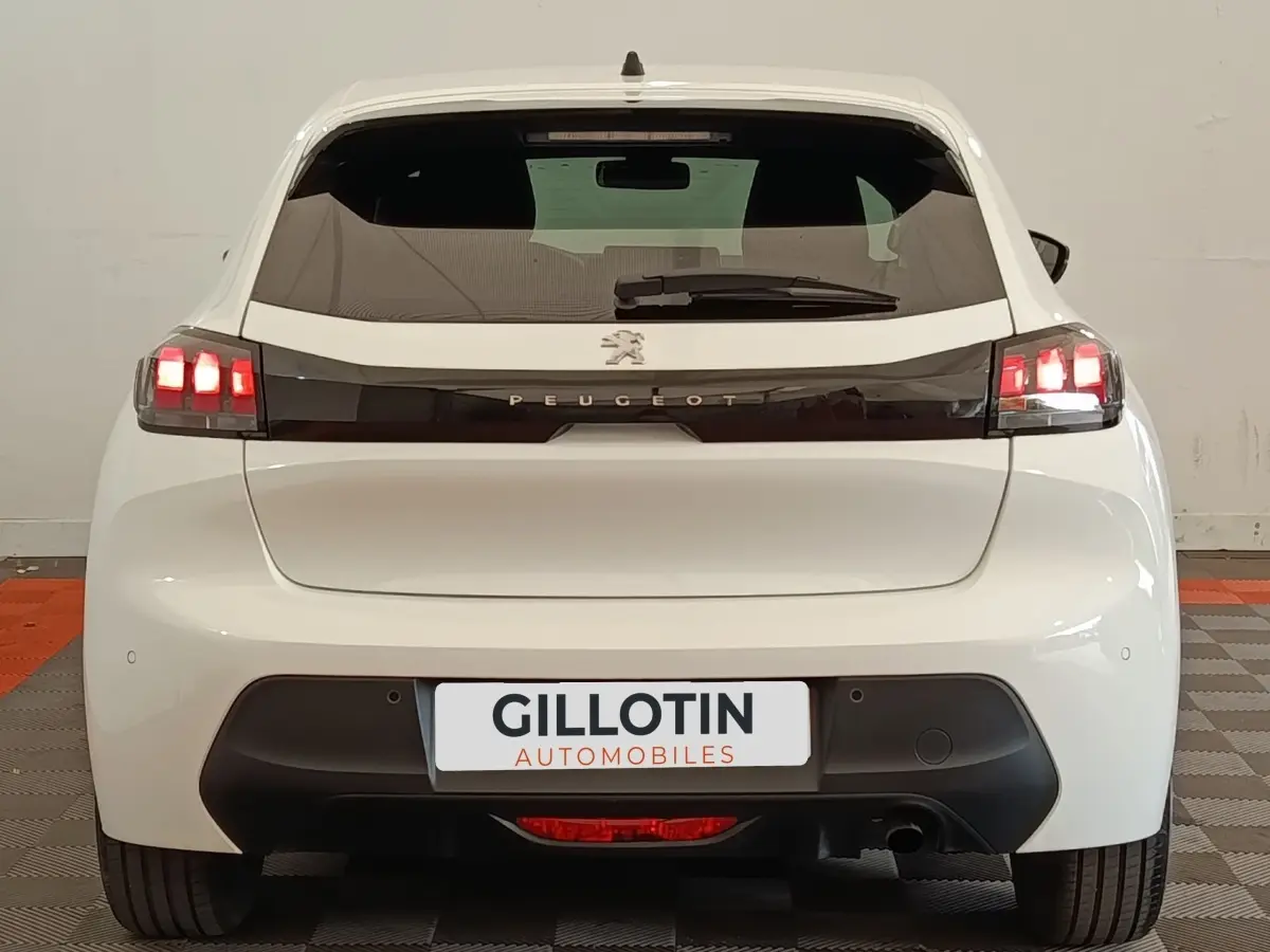 Vue arrière d'une Peugeot 208 blanche 2023 avec feux LED et bande noire distinctive sur le hayon.