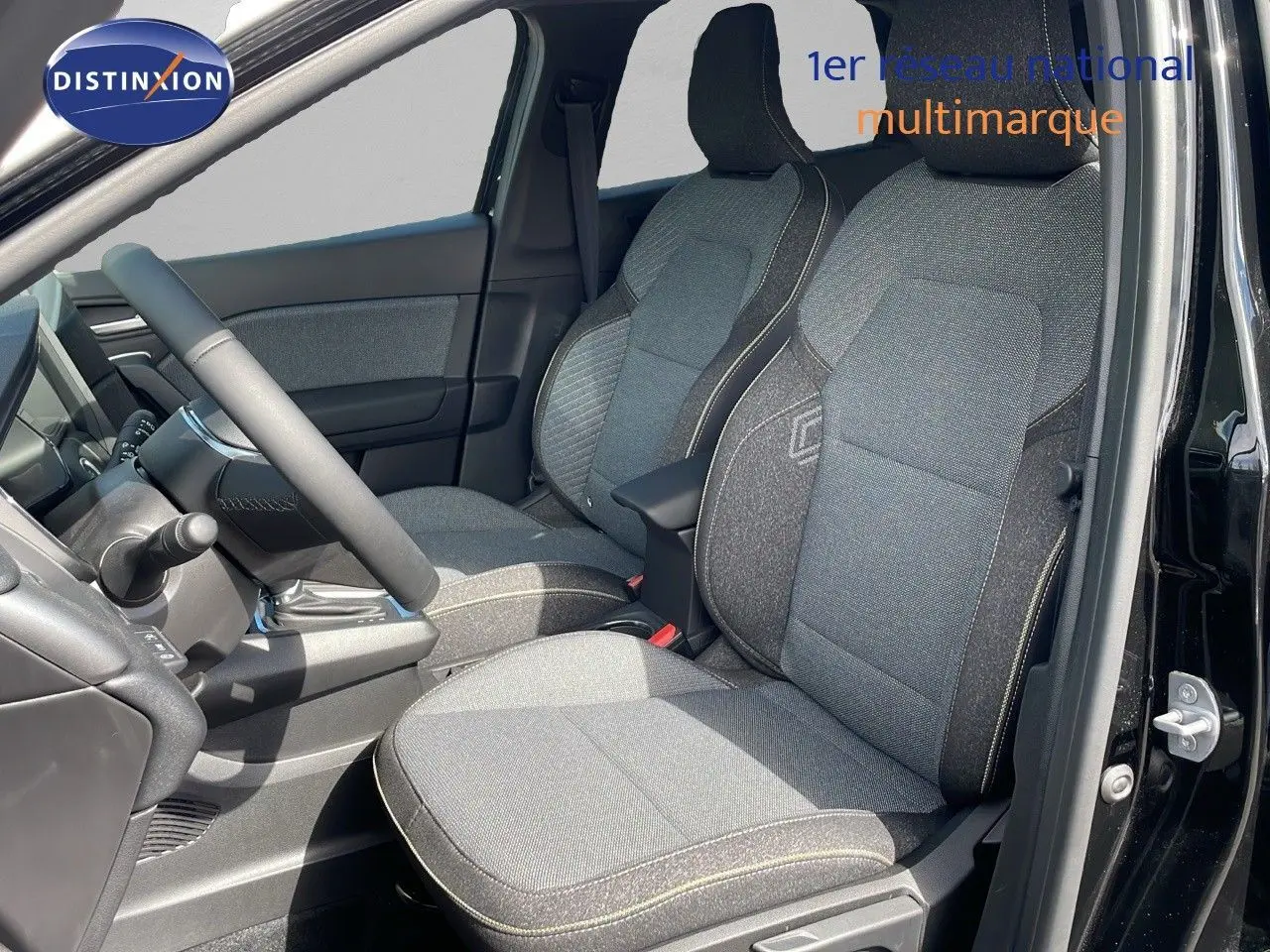 Vue intérieure côté conducteur du Renault Captur 2025, sièges tissu gris avec surpiqûres claires et tableau de bord noir.
