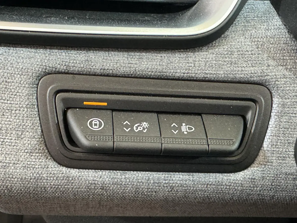Gros plan sur les commandes de réglage des phares et verrouillage, sur tableau de bord tissu gris clair Renault Clio 2025.