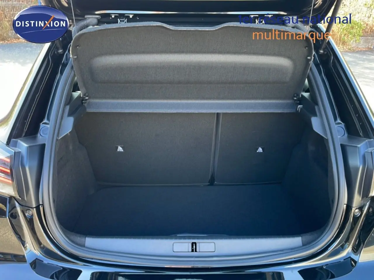 Coffre ouvert vu de l'arrière d'une Peugeot 208 Hybrid 110ch noir perla metal, espace de rangement visible et propre.