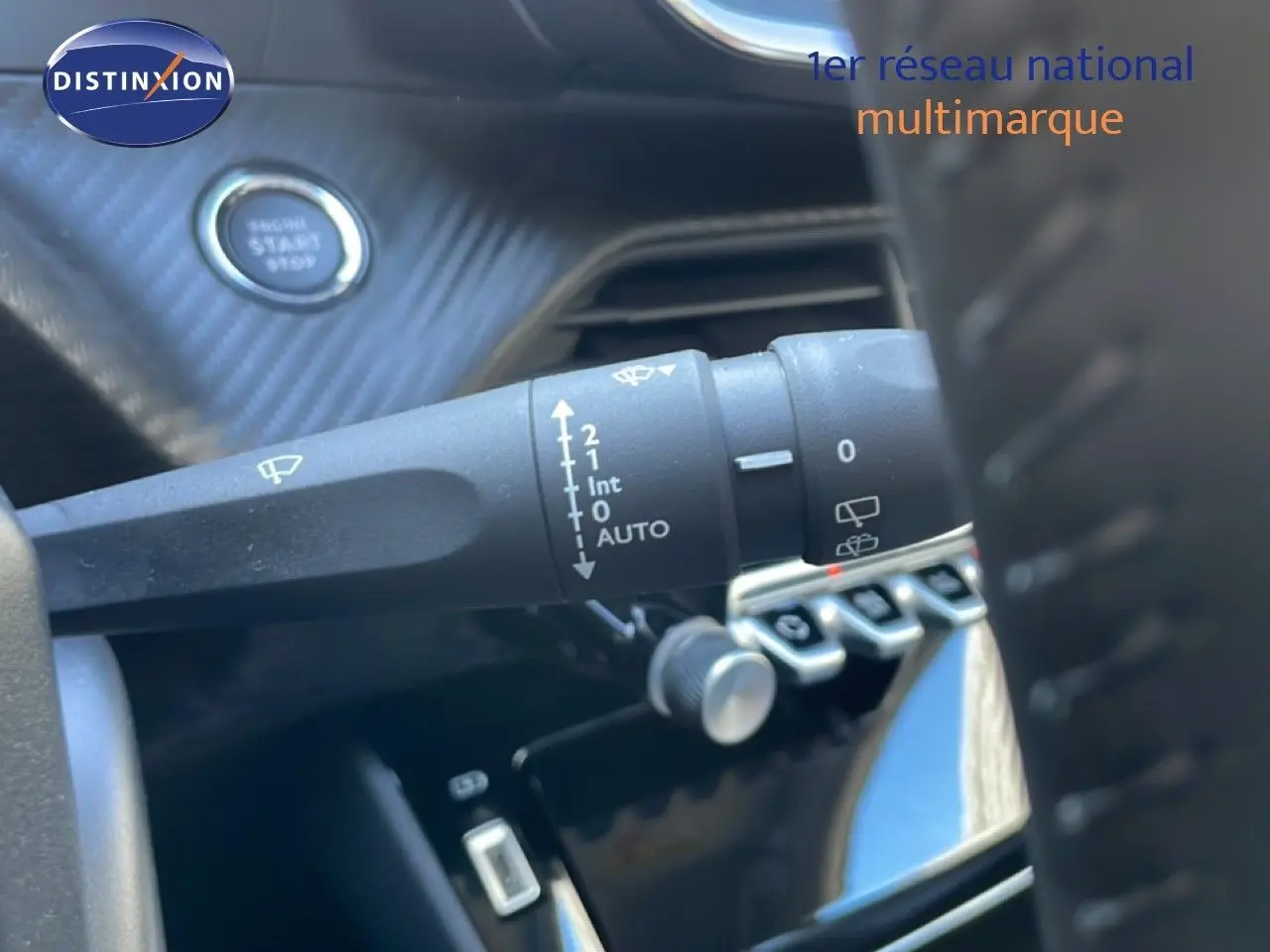 Gros plan sur la commande d’essuie-glace à gauche du volant d’une Peugeot 208 noire, avec bouton start en arrière-plan.