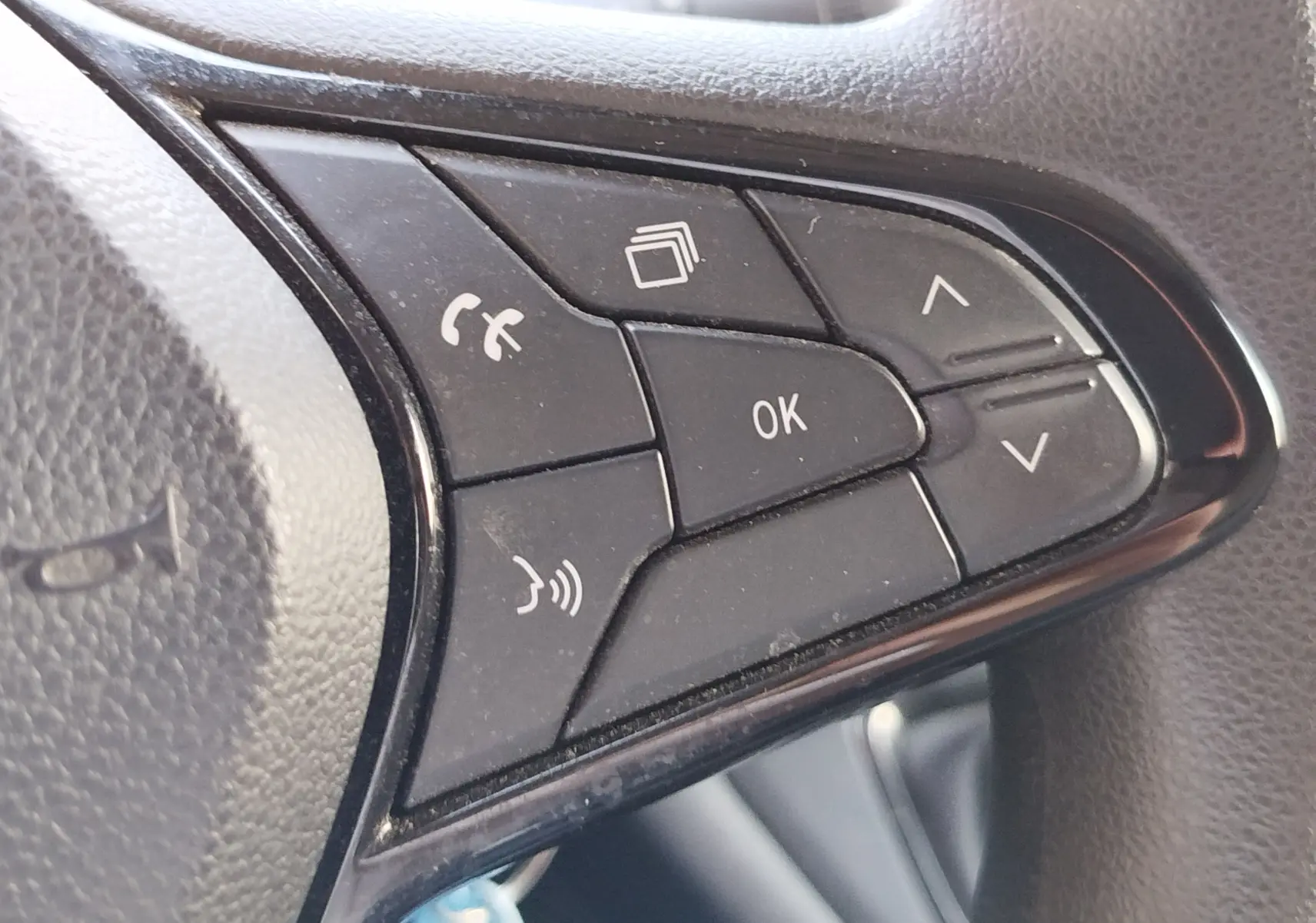 Gros plan sur les commandes noires du volant côté gauche du Renault Kangoo blanc, avec boutons de téléphone et navigation.