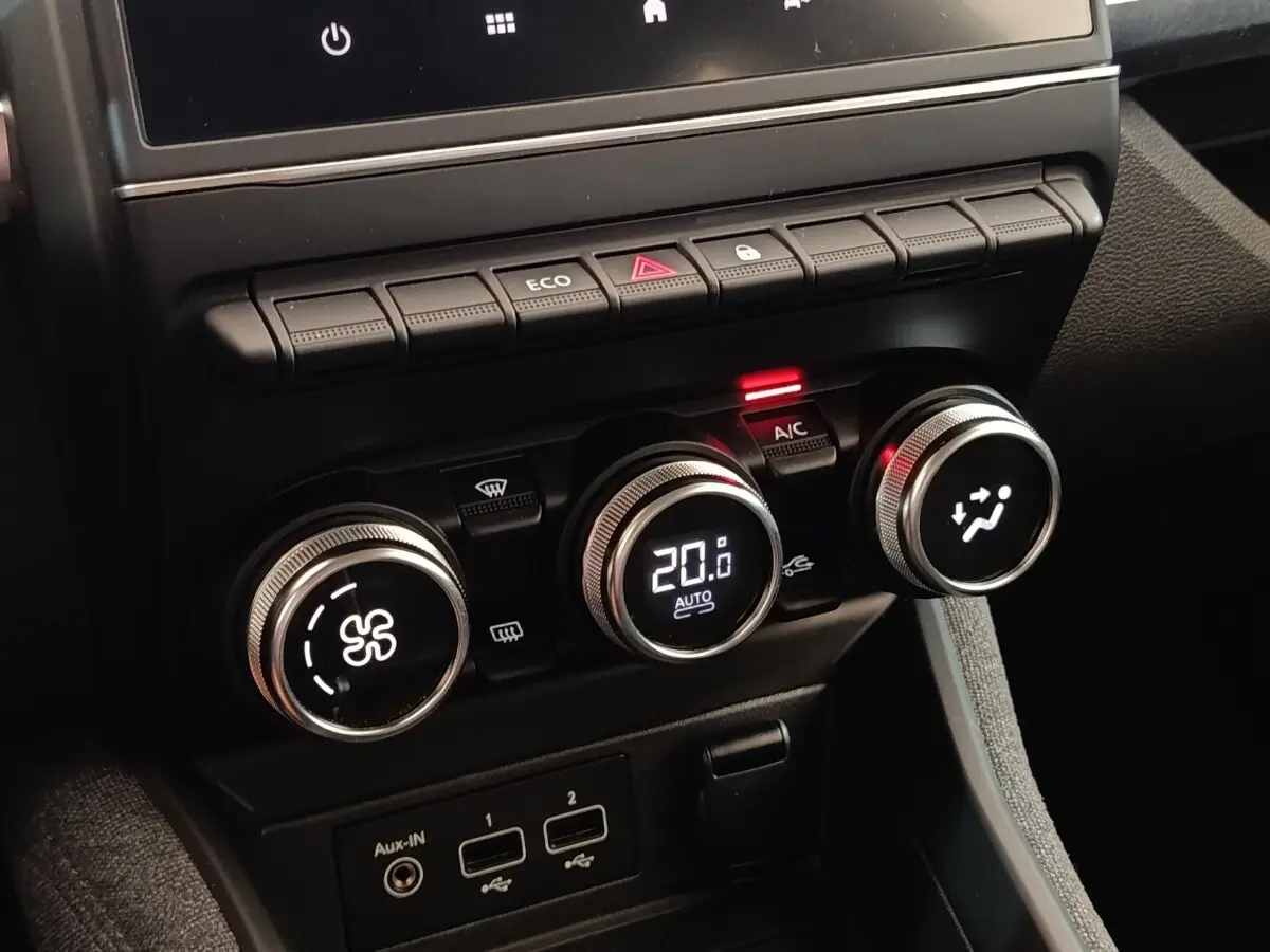 Gros plan sur la console centrale de la Renault ZOE blanche, avec commandes de climatisation digitales et boutons fonctionnels.