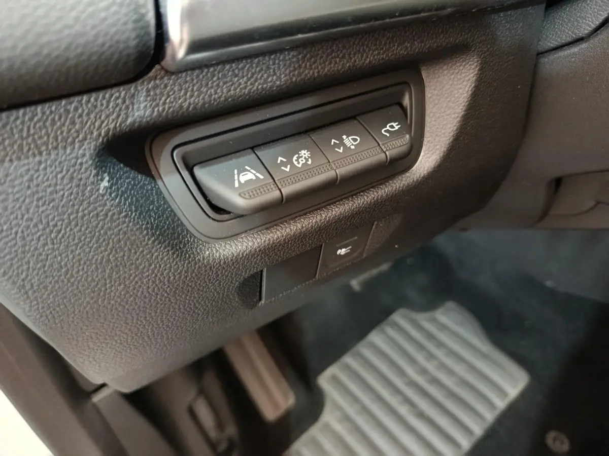 Gros plan sur les commandes d'assistance à la conduite à gauche du volant dans l'habitacle noir de la Renault ZOE blanche.