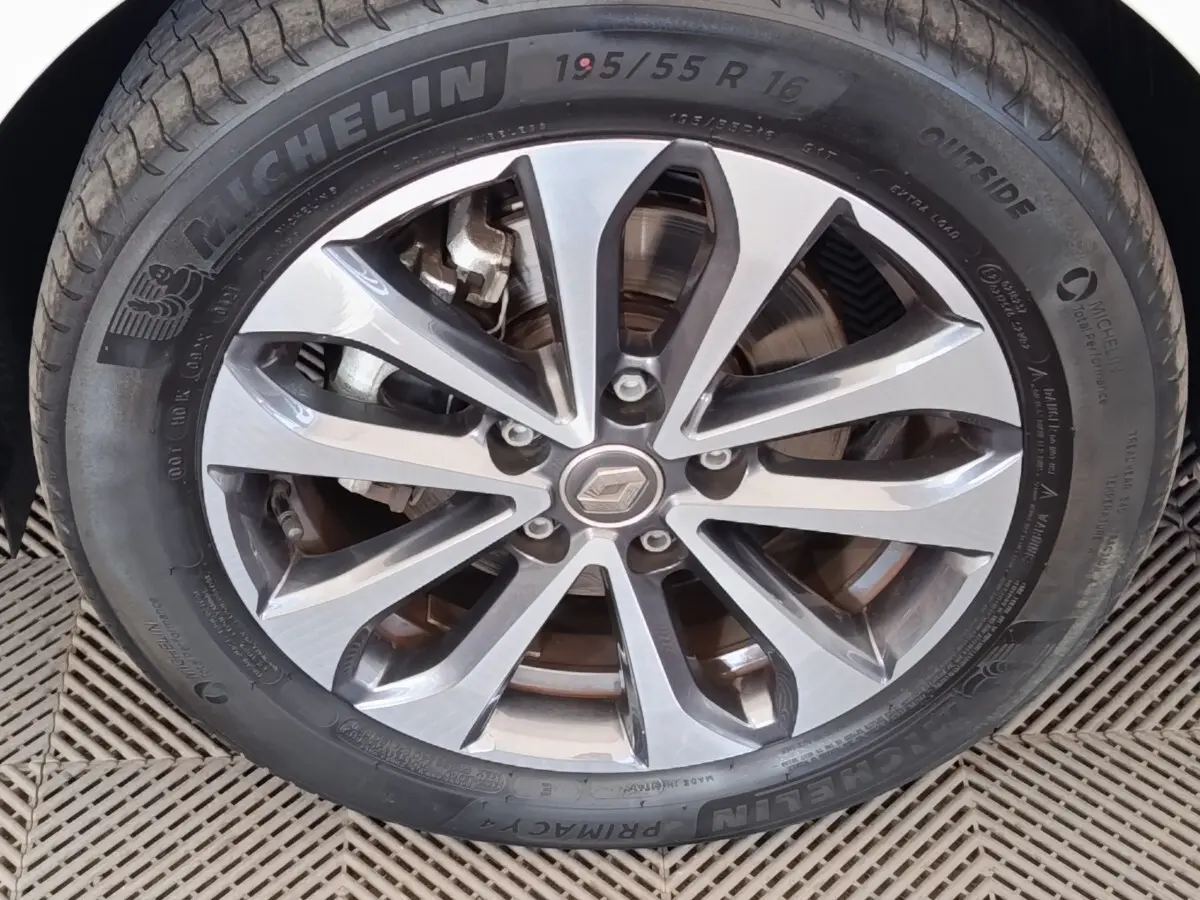 Gros plan sur la jante alliage gris et noir avec logo Renault au centre, montée sur pneu Michelin d’une Renault ZOE blanche.