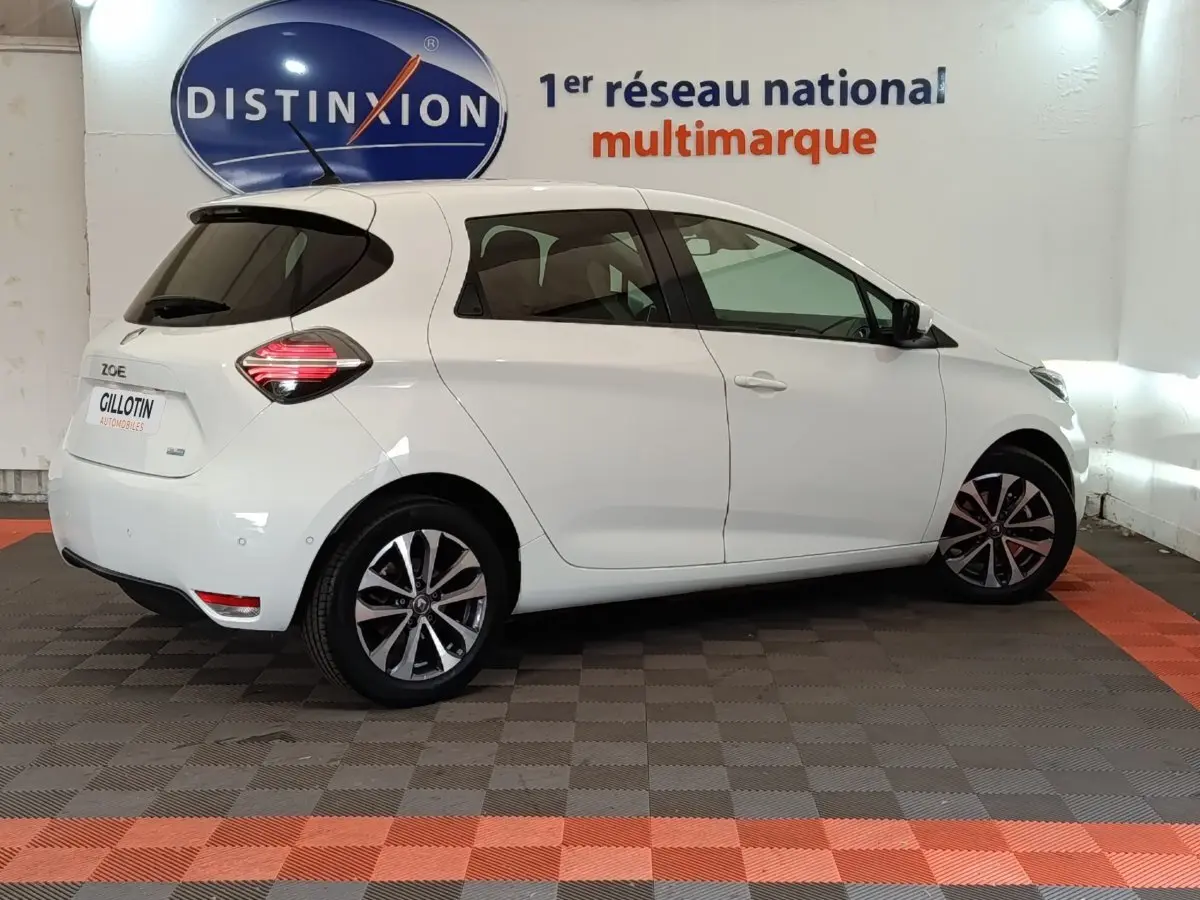 Renault ZOE Intens R110 blanc vue de profil côté droit en intérieur avec jantes alliage et feux arrière LED allumés.
