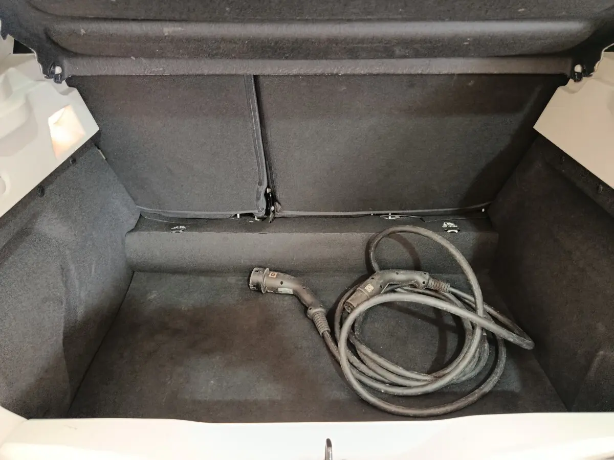 Coffre ouvert d'une Renault ZOE blanche avec câble de recharge électrique enroulé à l'intérieur.