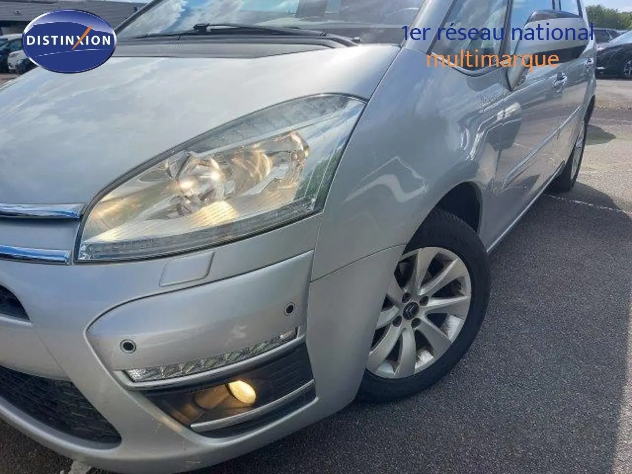 Vue 3/4 avant droit d'une Citroën C4 Picasso gris alu métal avec feux allumés et jantes alliage visibles.