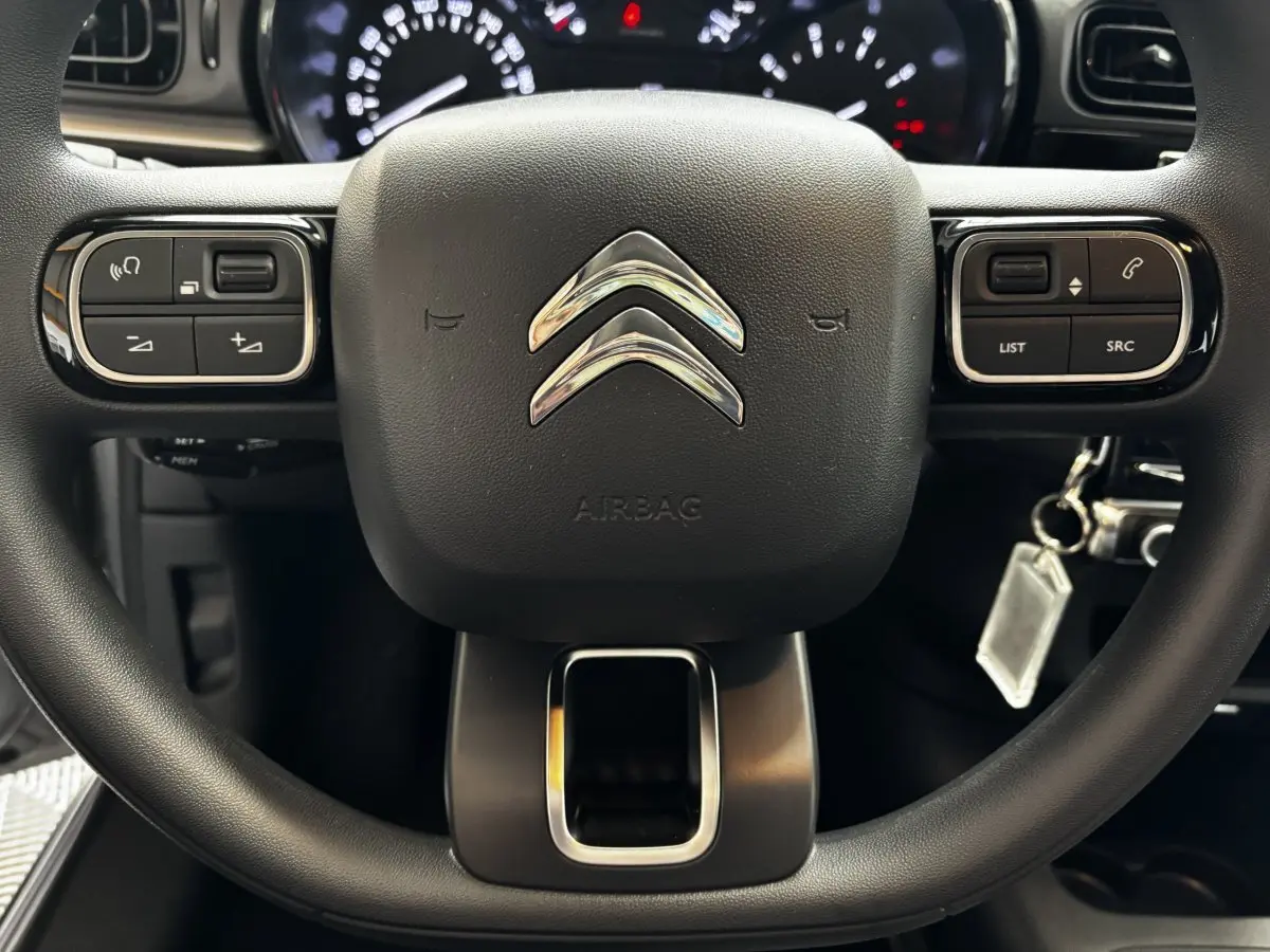 Gros plan sur le volant multifonctions noir de la Citroën C3 PureTech 110, avec commandes intégrées et logo chromé central.