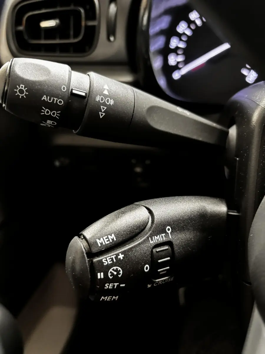 Gros plan sur les commandes de régulateur de vitesse et feux du tableau de bord d'une Citroën C3 2024 gris foncé.