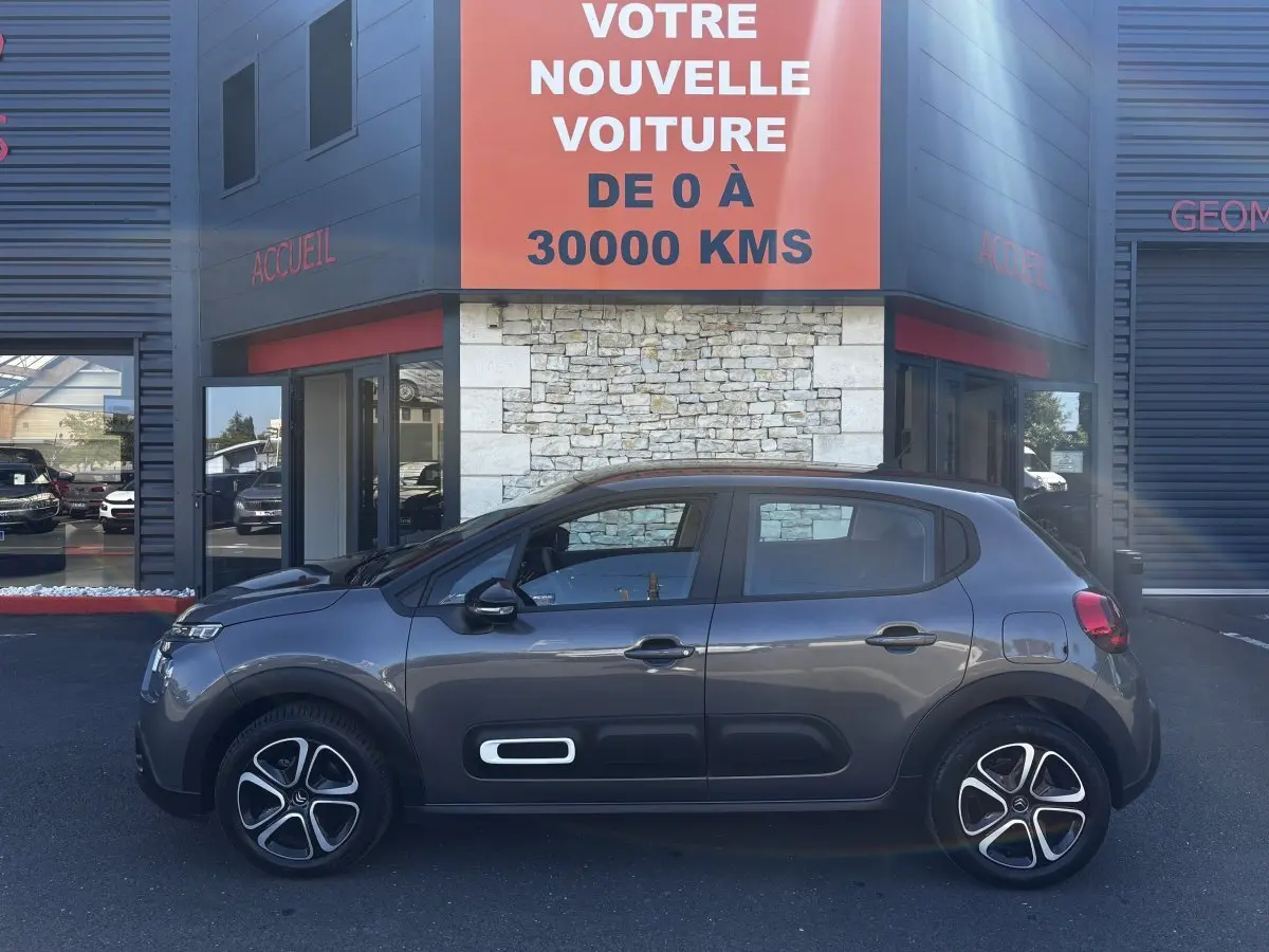 Profil côté gauche de la Citroën C3 2024 gris foncé avec ses jantes distinctives et protections latérales noires.
