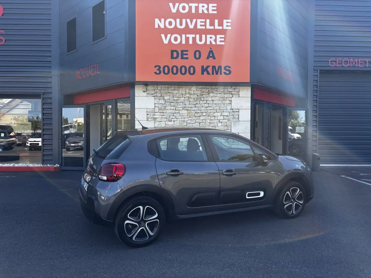 Citroën C3 gris foncé vue de profil côté droit, avec protections latérales blanches et jantes stylisées.
