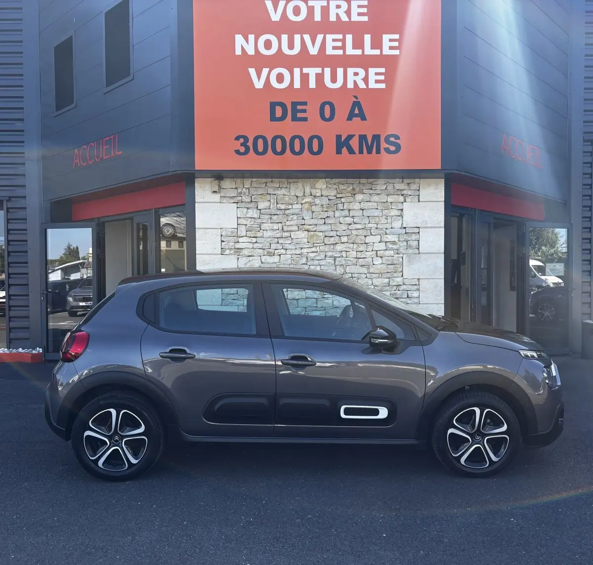 Vue profil côté gauche d'une Citroën C3 gris foncé 2024 avec protections latérales noires et jantes stylisées.