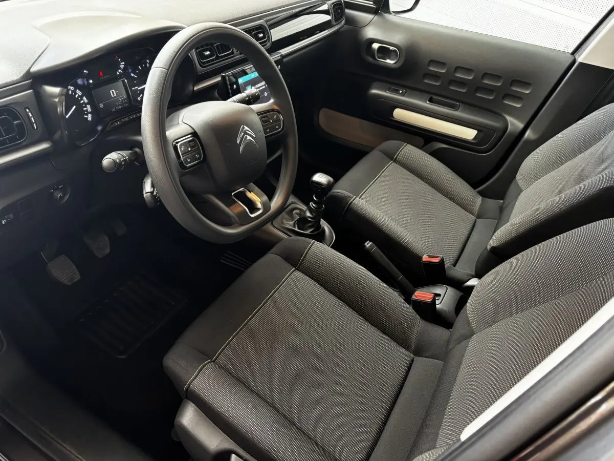 Intérieur avant droit de la Citroën C3 2024 gris foncé, volant multifonction et boîte manuelle visibles.