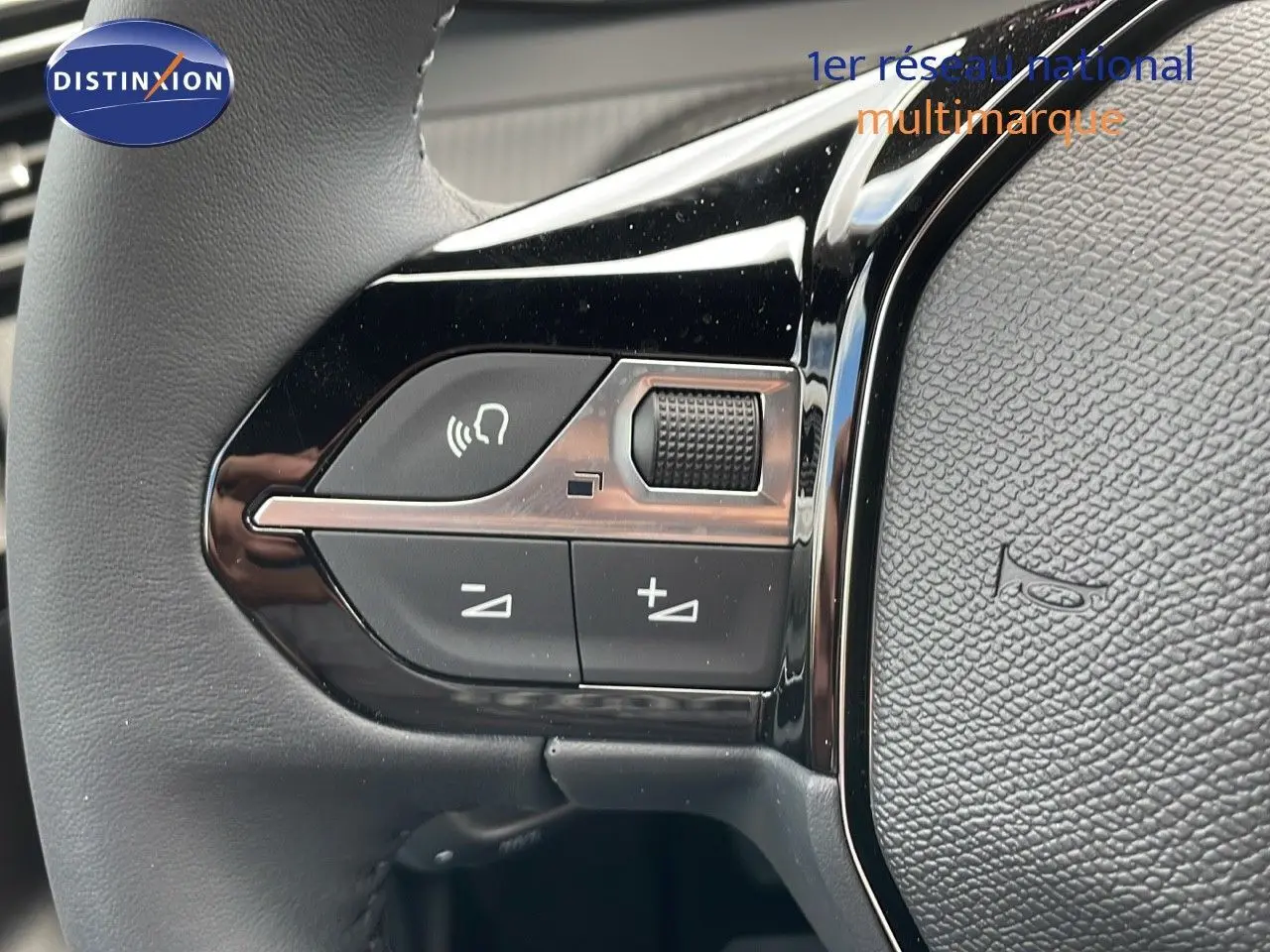 Gros plan sur les commandes de volume au volant d'une Peugeot 2008 noire, mettant en valeur les boutons tactiles et la molette.