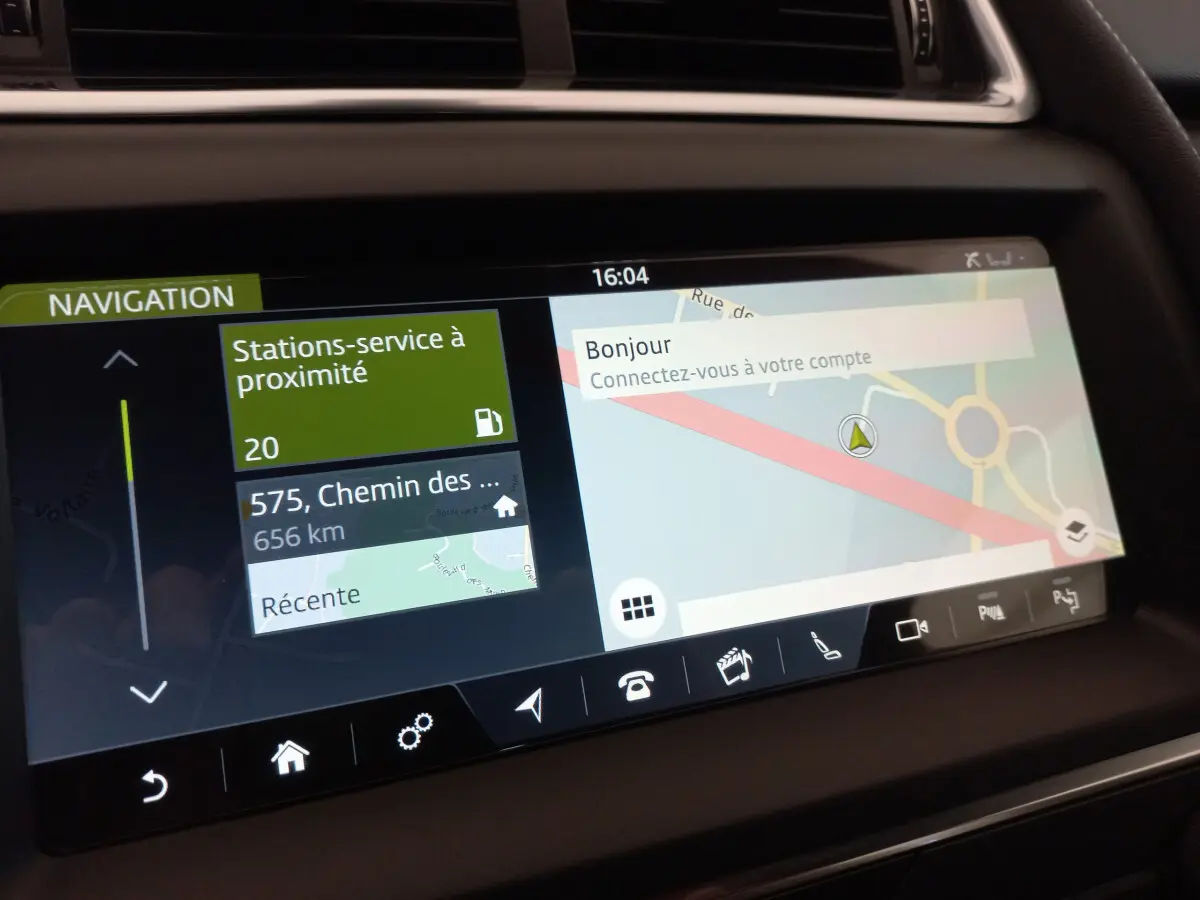 Écran tactile de navigation du tableau de bord du Jaguar E-PACE blanc, affichant carte et stations-service à proximité.
