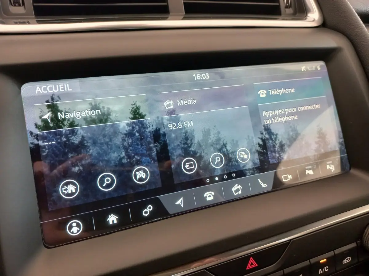 Écran tactile central du tableau de bord du Jaguar E-PACE blanc, affichant navigation et média à 16h03.