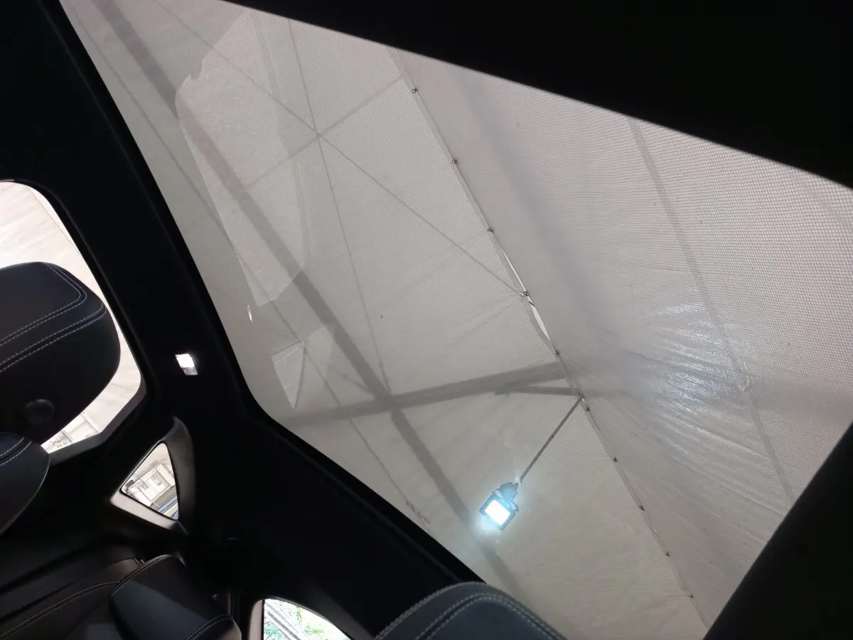 Toit panoramique en verre vu de l'intérieur arrière gauche du Jaguar E-PACE blanc 2019 avec ciel couvert.