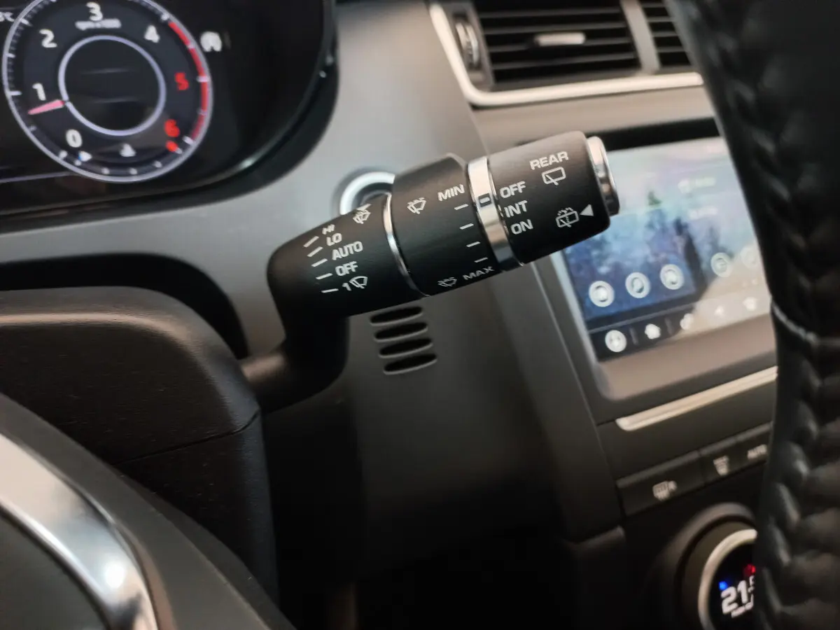 Gros plan sur la commande d’essuie-glace à gauche du volant dans l’habitacle sombre d’une Jaguar E-PACE blanc.