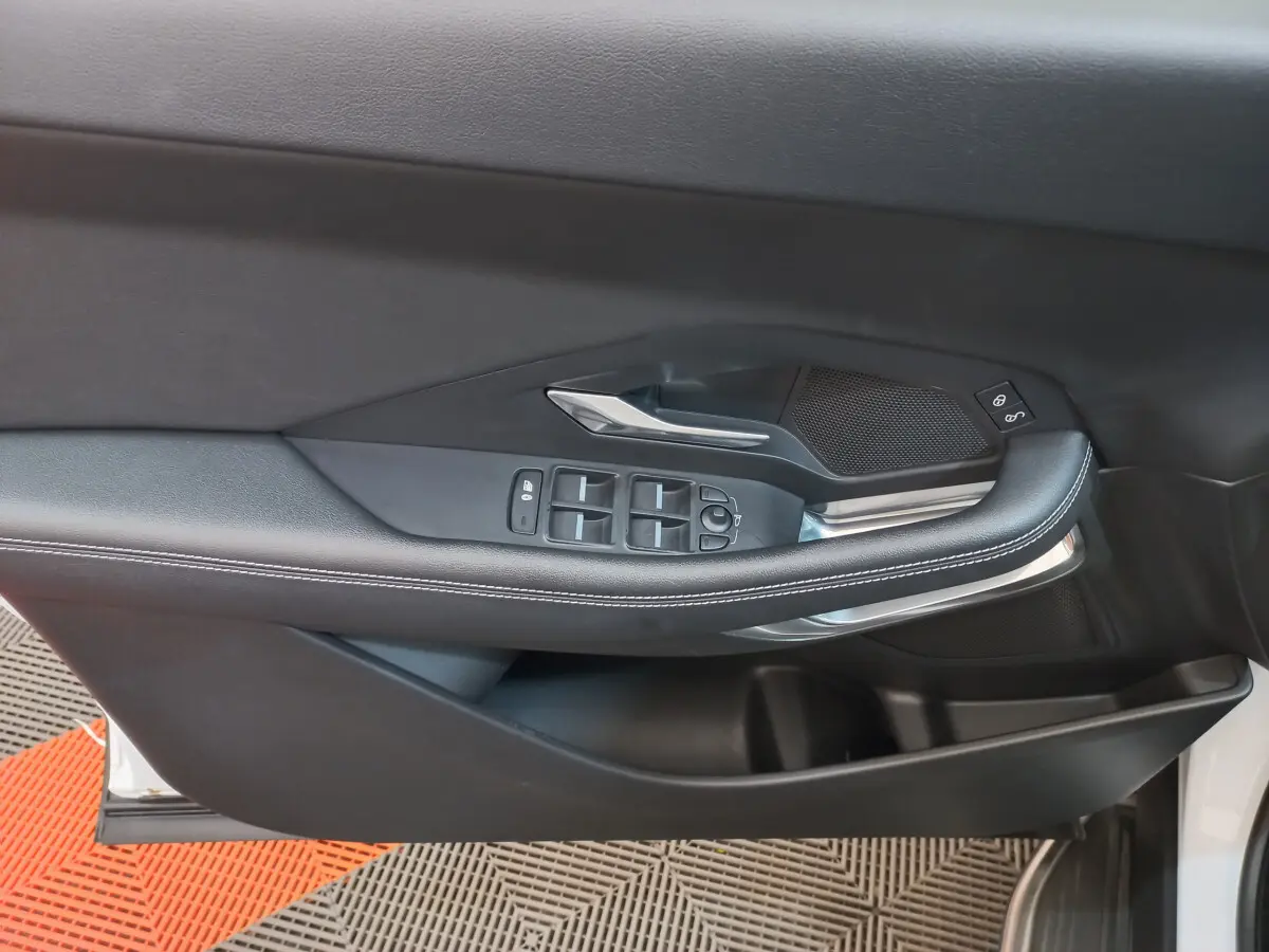 Gros plan sur la porte côté gauche de la Jaguar E-PACE blanche, avec commandes des vitres et poignée argentée.