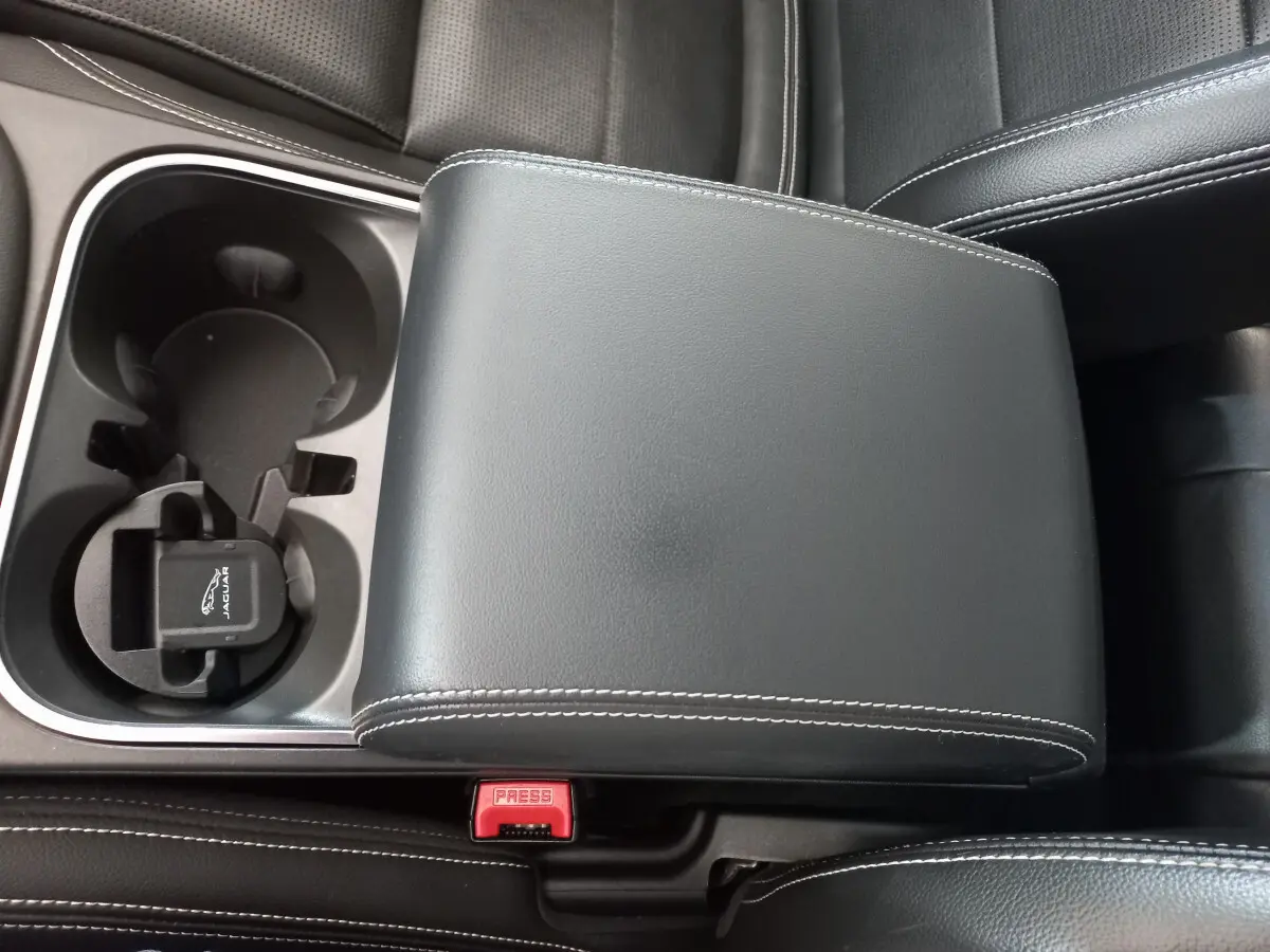 Gros plan sur l'accoudoir central en cuir noir avec surpiqûres blanches et porte-gobelets du Jaguar E-PACE blanc 2019.