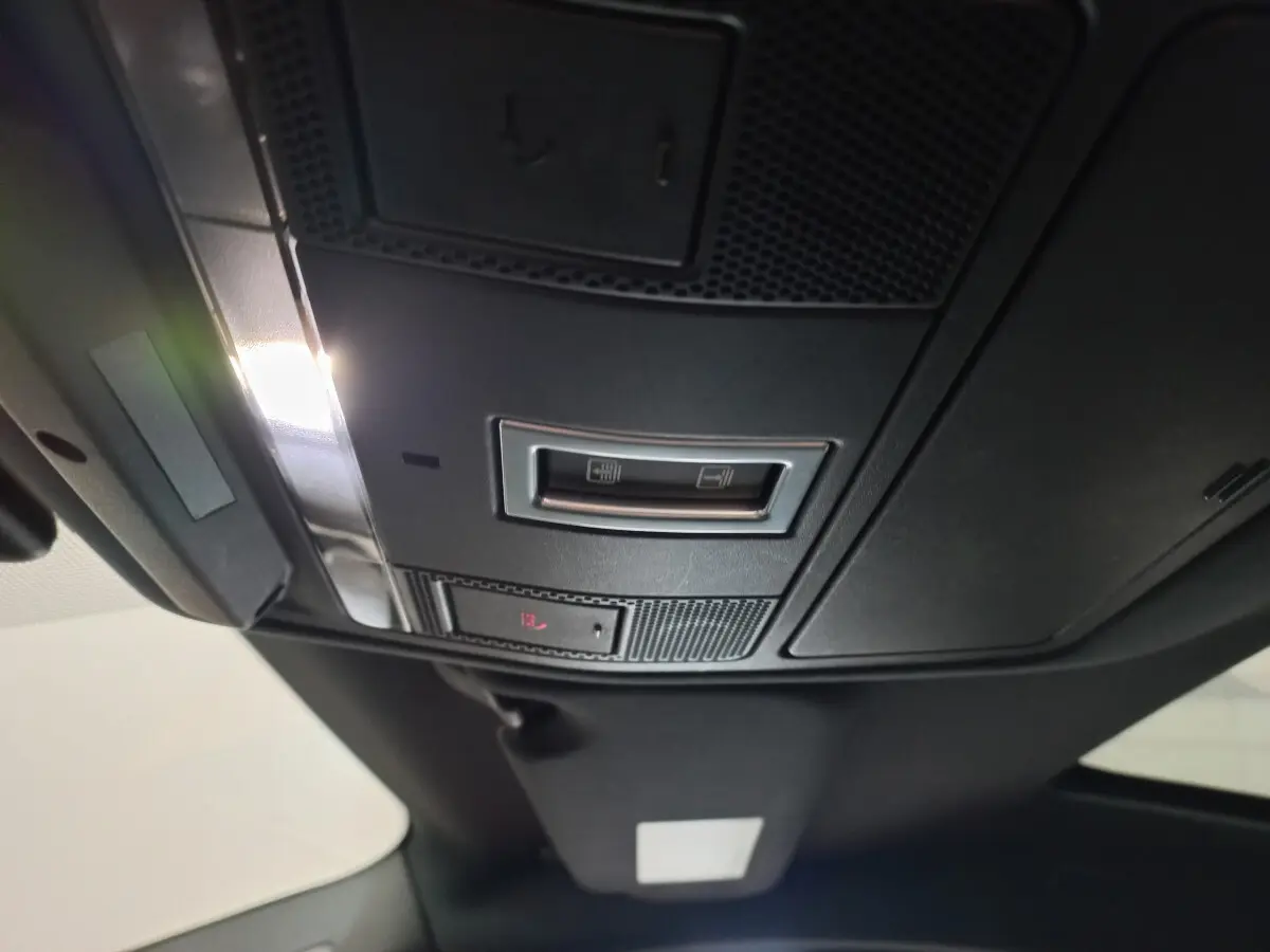 Vue en contre-plongée du panneau de commande de toit noir du Jaguar E-PACE blanc, avec éclairage intérieur allumé.
