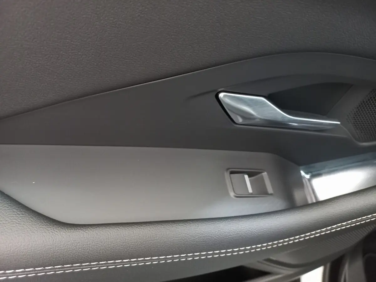 Poignée de porte intérieure côté gauche de la Jaguar E-PACE blanc, avec surpiqûres blanches et insert métal brossé.