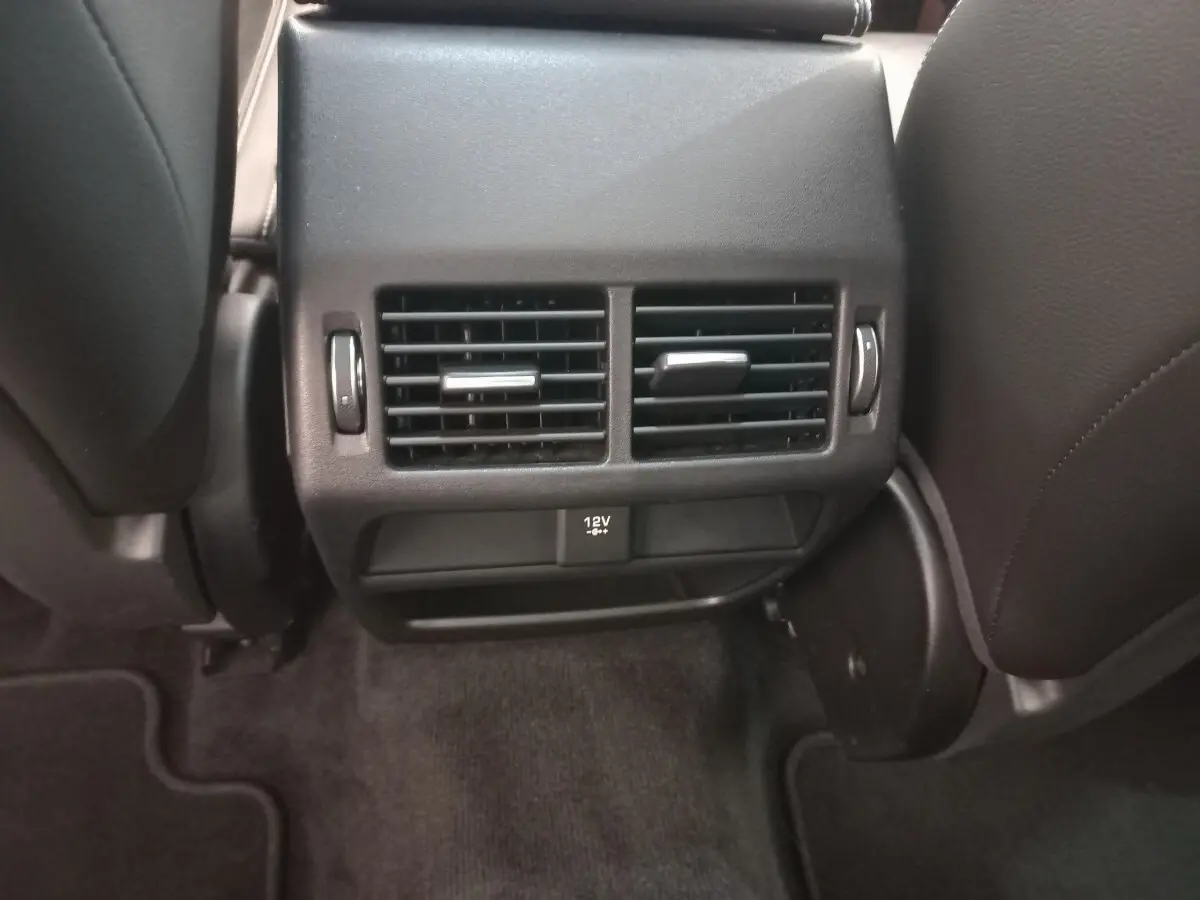 Vue rapprochée des aérateurs arrière noirs et prise 12V entre les sièges avant d'une Jaguar E-PACE blanche.