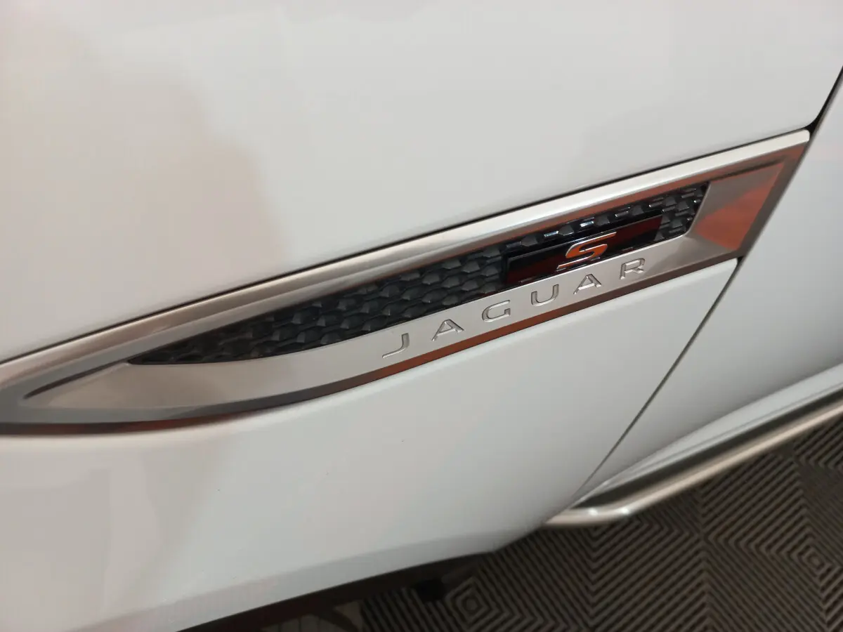 Gros plan sur l'emblème latéral "S" noir et orange du côté droit d'une Jaguar E-PACE blanche.