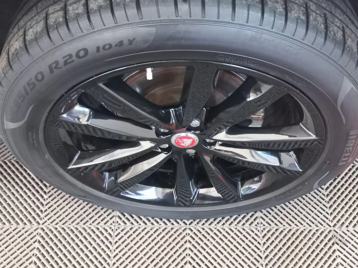 Gros plan sur la jante noire brillante avec logo Jaguar rouge d'un Jaguar E-PACE blanc, pneu Pirelli visible.