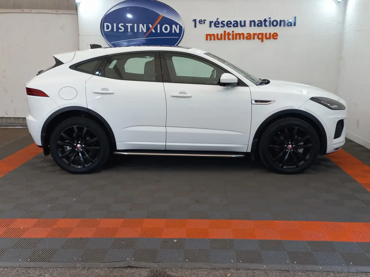 Jaguar E-PACE blanc vue de profil côté gauche avec jantes noires dans un showroom multimarque.