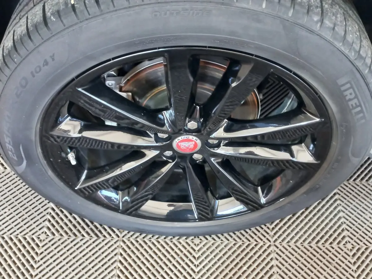 Gros plan sur la jante noire brillante d'une Jaguar E-PACE blanche, mettant en valeur le logo central rouge.