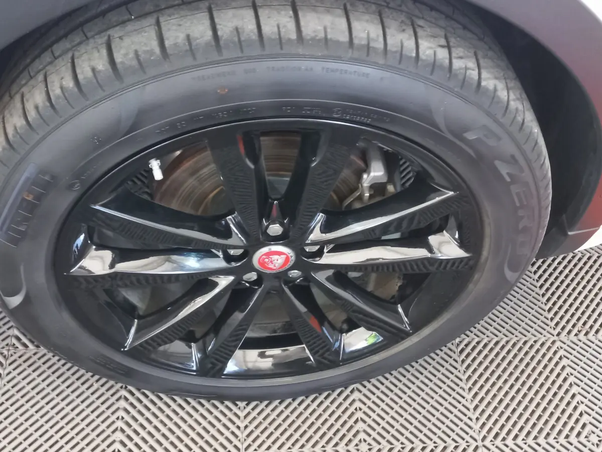 Gros plan sur la roue avant droite du Jaguar E-PACE blanc, jante noire brillante avec logo Jaguar rouge au centre.