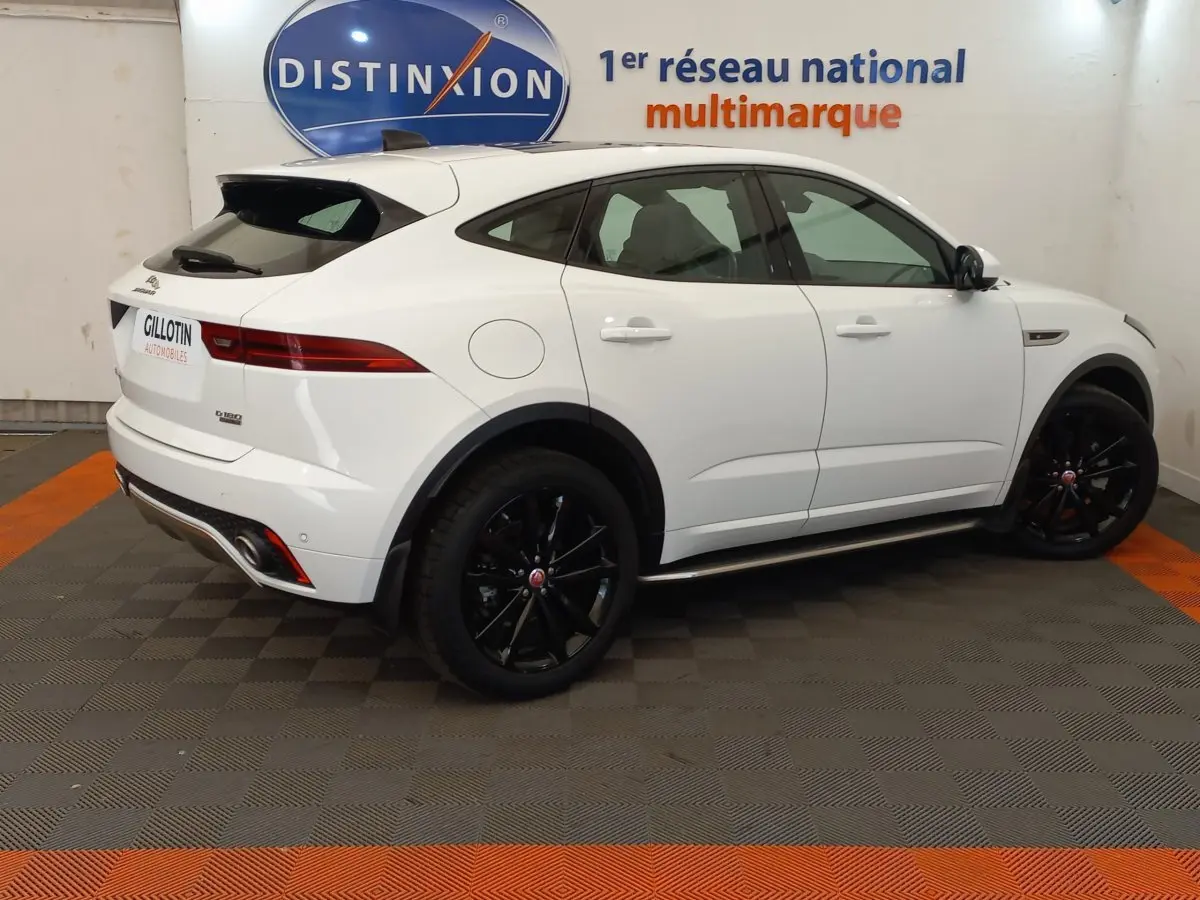Vue de profil côté gauche d'un Jaguar E-PACE blanc avec jantes noires dans un showroom multimarque.