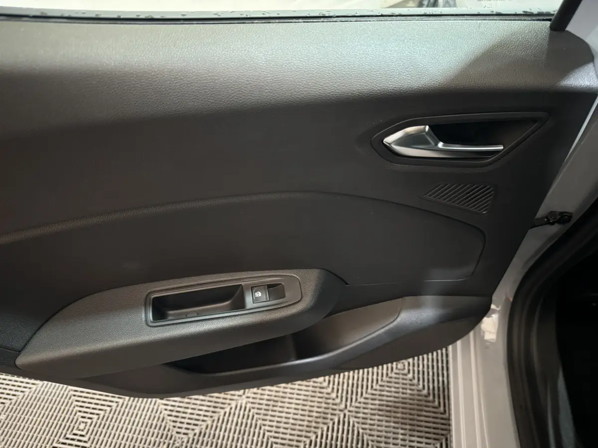 Intérieur de la porte côté droit gris foncé de la Renault Clio 2025 avec poignée argentée et commande de vitre électrique.