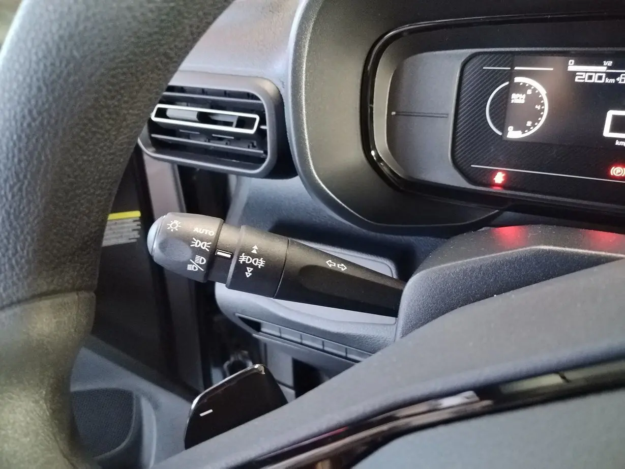 Gros plan sur la commande des feux et clignotants à gauche du volant dans le tableau de bord du Citroën Berlingo gris acier 2025.