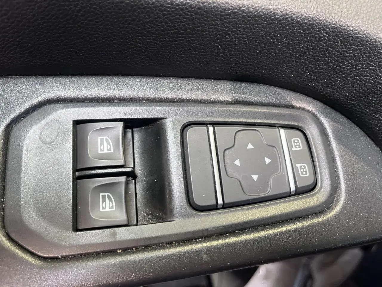 Gros plan sur les commandes de lève-vitres et réglage des rétroviseurs du Renault Trafic Fourgon gris foncé.