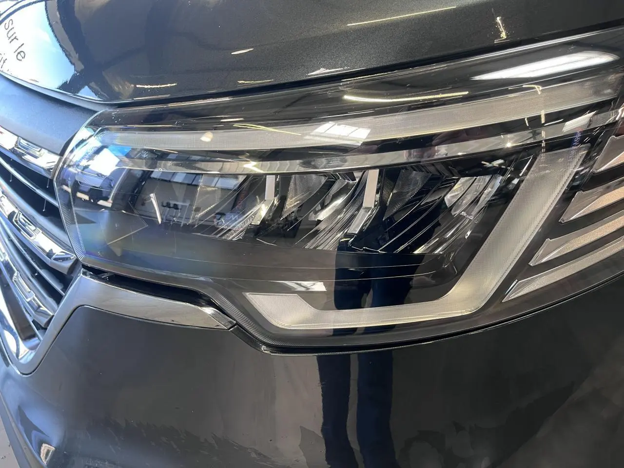 Gros plan sur le phare avant droit du Renault Trafic Fourgon gris foncé, avec calandre et détails LED visibles.