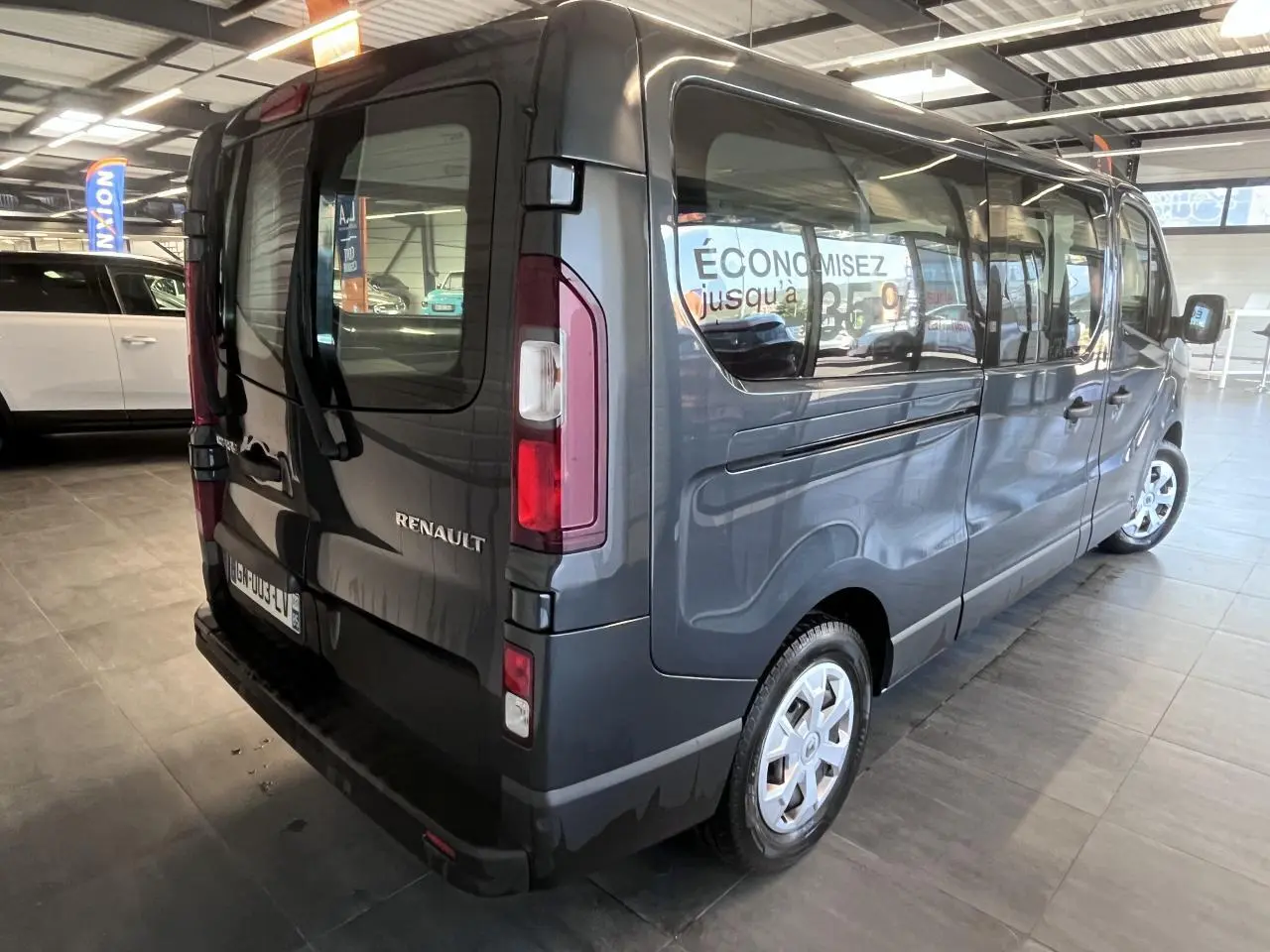 Vue 3/4 arrière droite d’un Renault Trafic Fourgon gris foncé avec vitres latérales teintées en showroom.