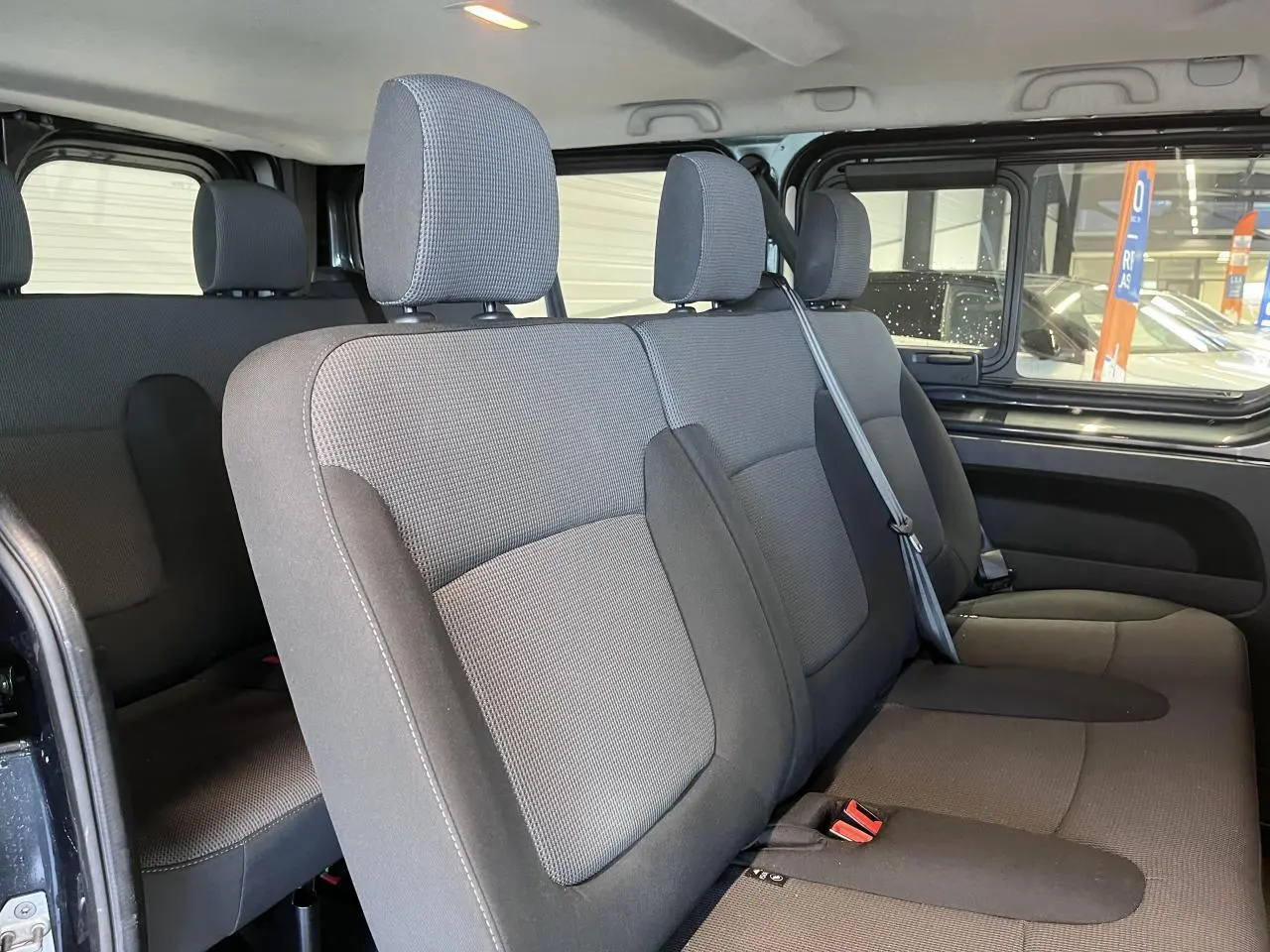 Vue intérieure côté droit sur la banquette arrière grise du Renault Trafic Fourgon 2023 avec vitres latérales ouvertes.