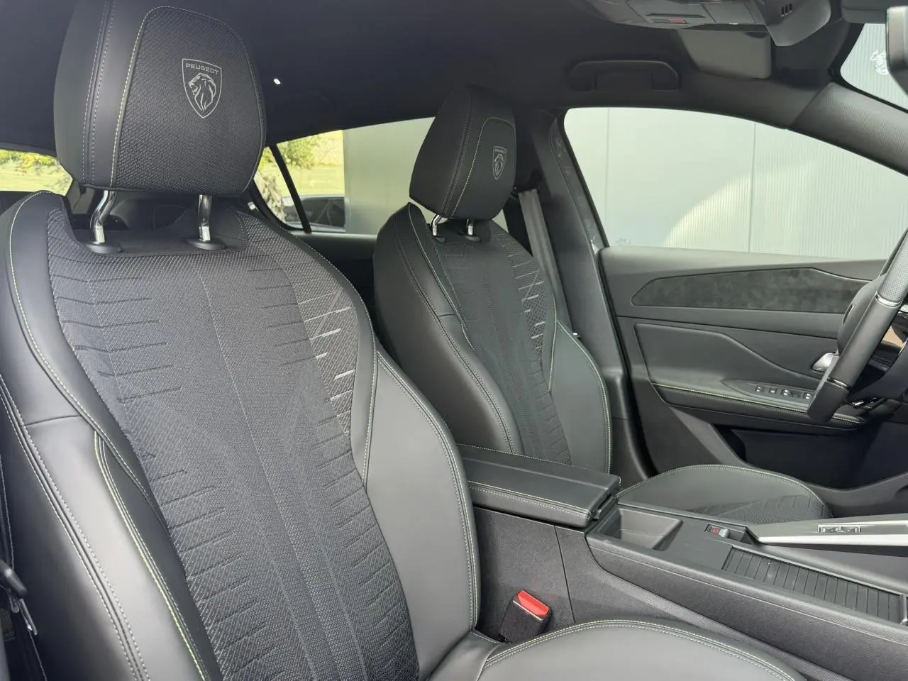Vue intérieure côté droit des sièges avant noirs avec surpiqûres vert Adamite et logo Peugeot embossé sur les appuie-têtes.